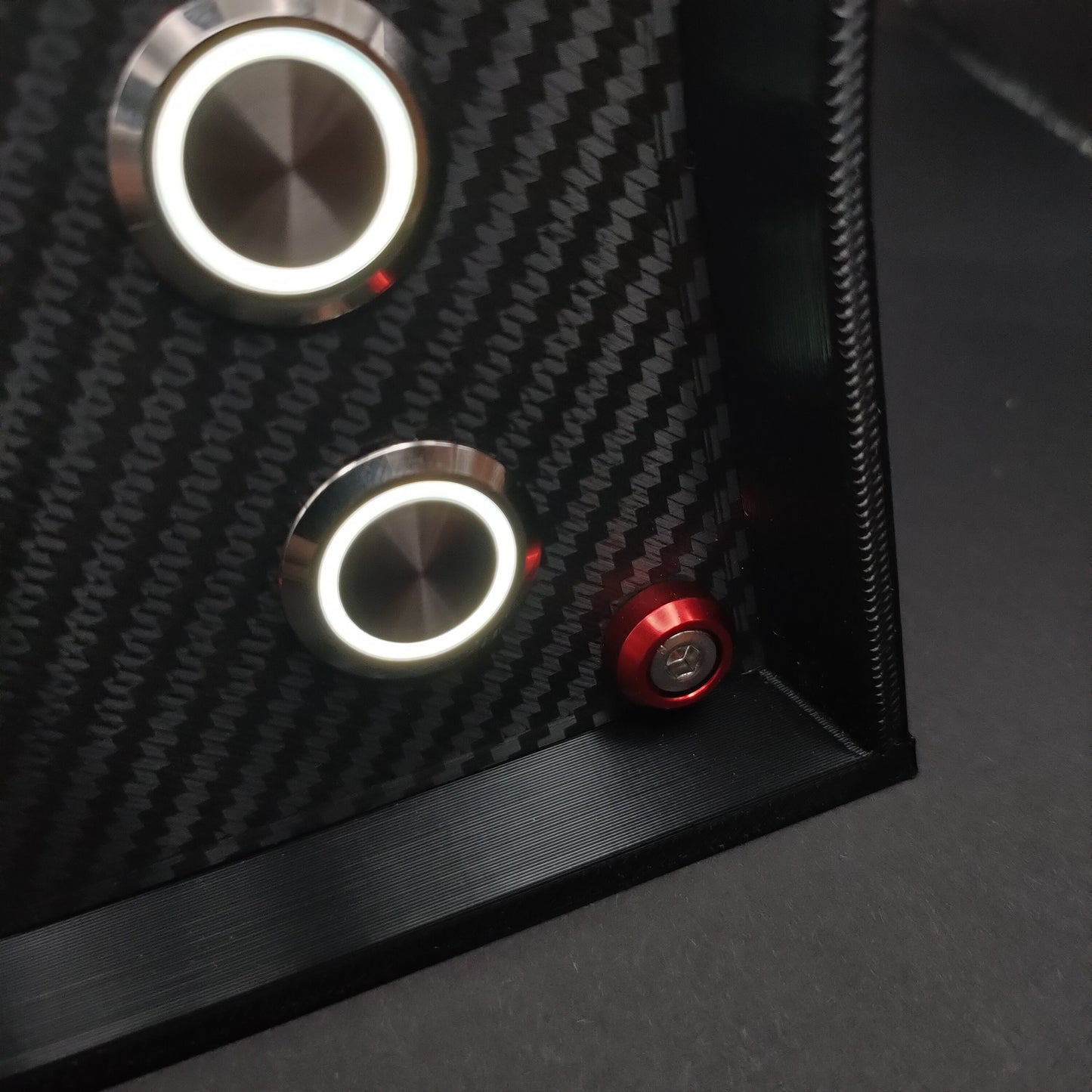 Detail shot of red anodised aluminium bolt trim and white LED illuminated chrome buttons on carbon.