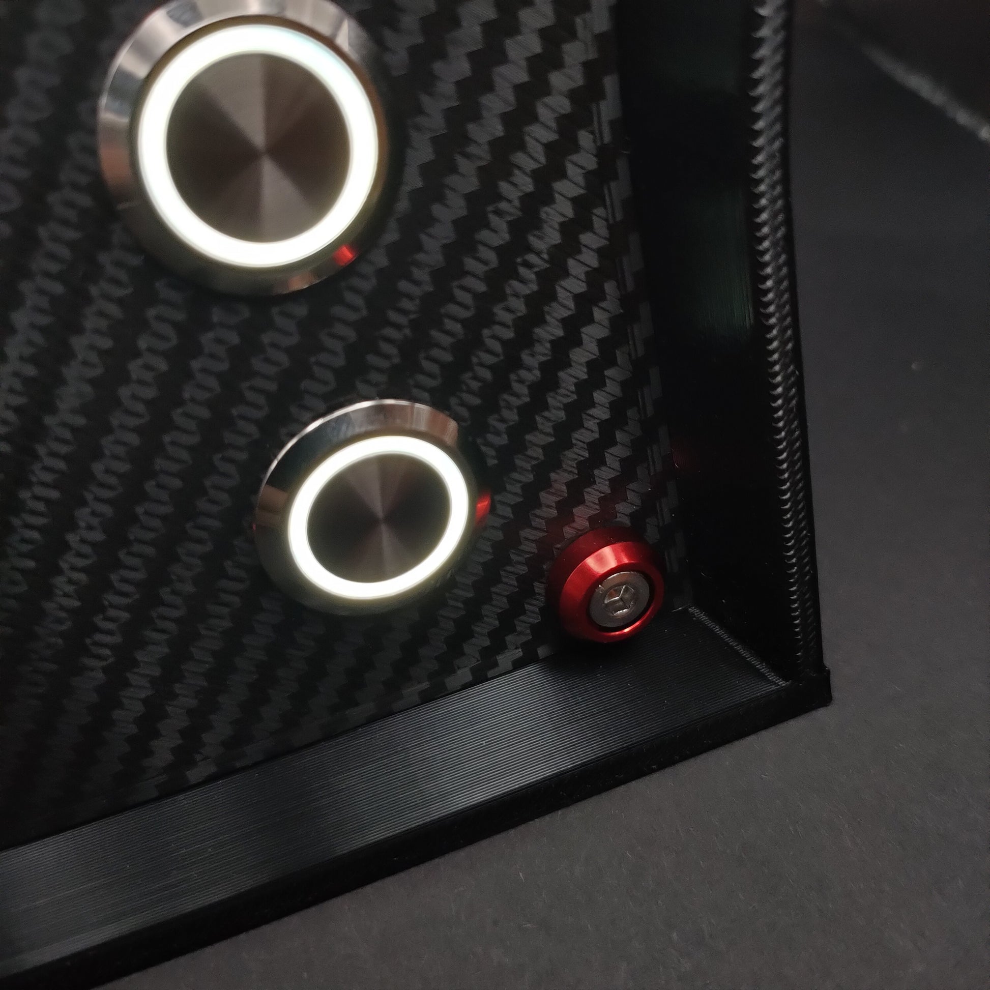 Detail shot of red anodised aluminium bolt trim and white LED illuminated chrome buttons on carbon.