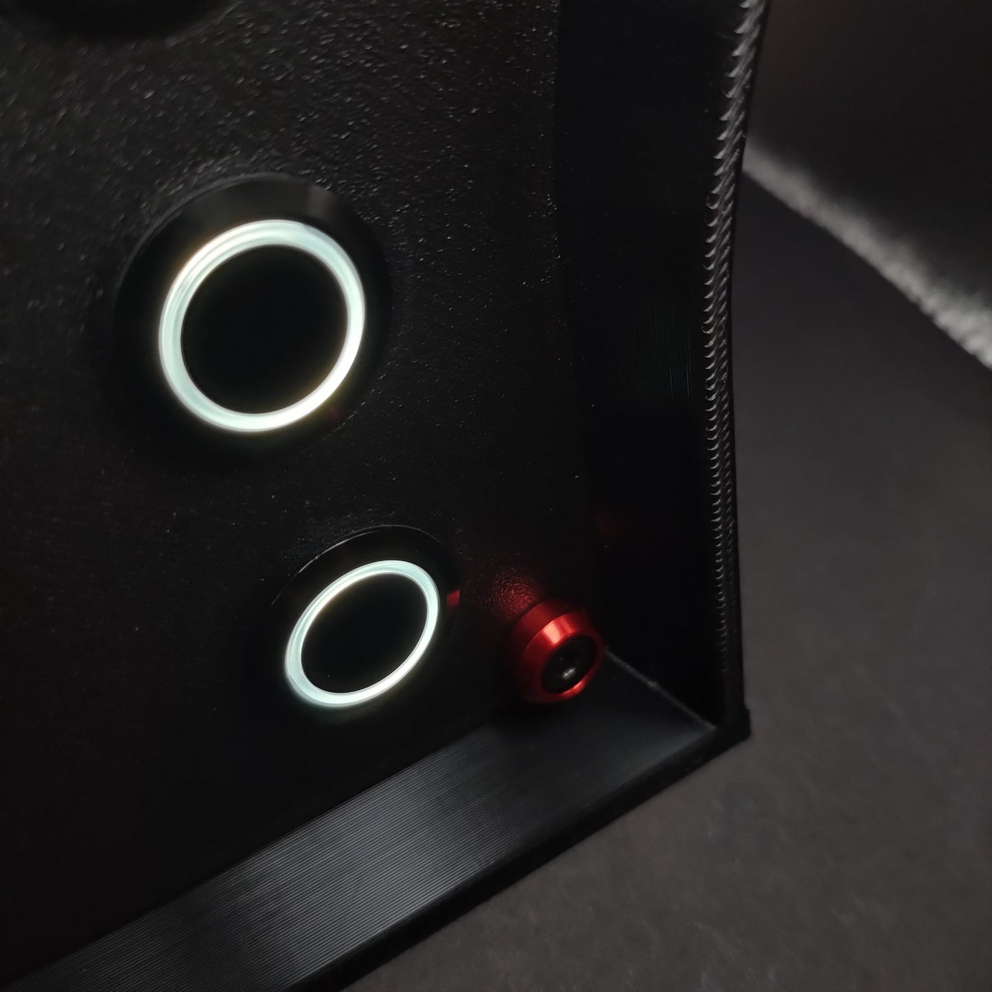 Detail shot of the black aluminium push buttons with white LED rings on matte black with red anodised aluminium trim.