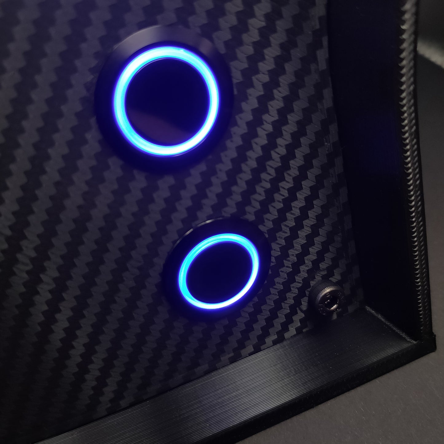 Detail shot of black chrome momentary push buttons with blue LED rings on a carbon fibre faceplate.