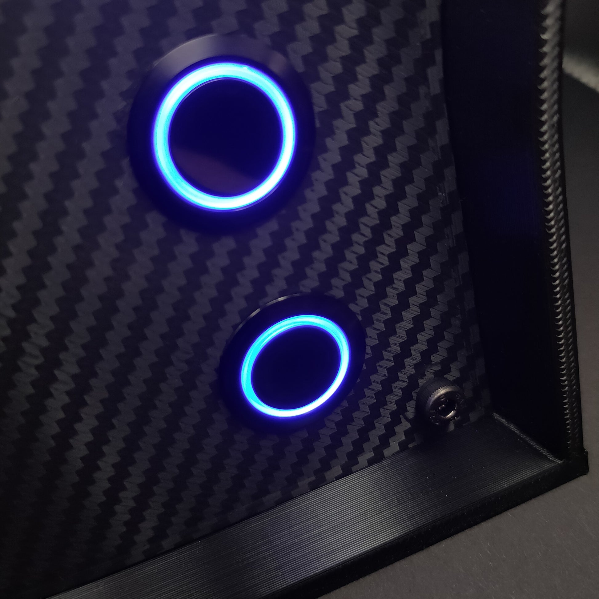 Detail shot of black chrome momentary push buttons with blue LED rings on a carbon fibre faceplate.