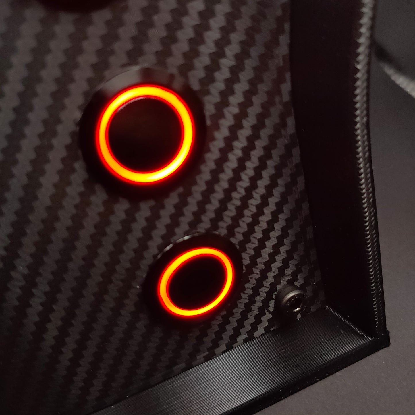 Close-up of black chrome momentary push buttons with red LED rings on a carbon fibre faceplate.